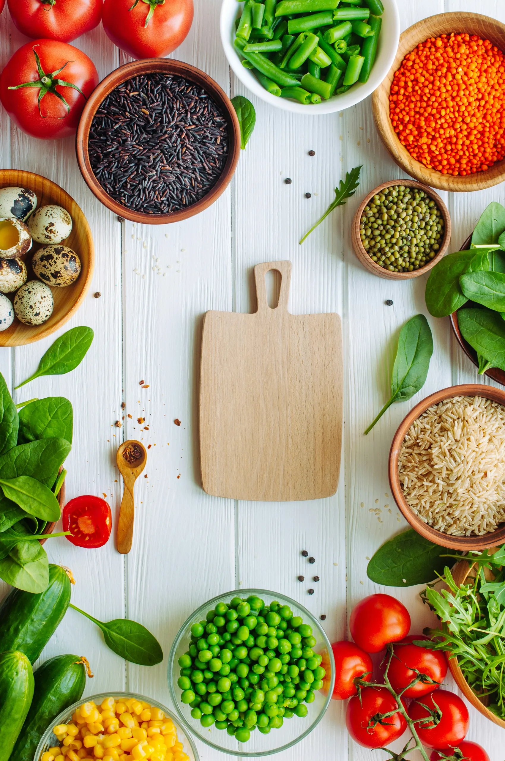 Verduras frescas, cereales y legumbres dispuestos alrededor de una tabla de cortar